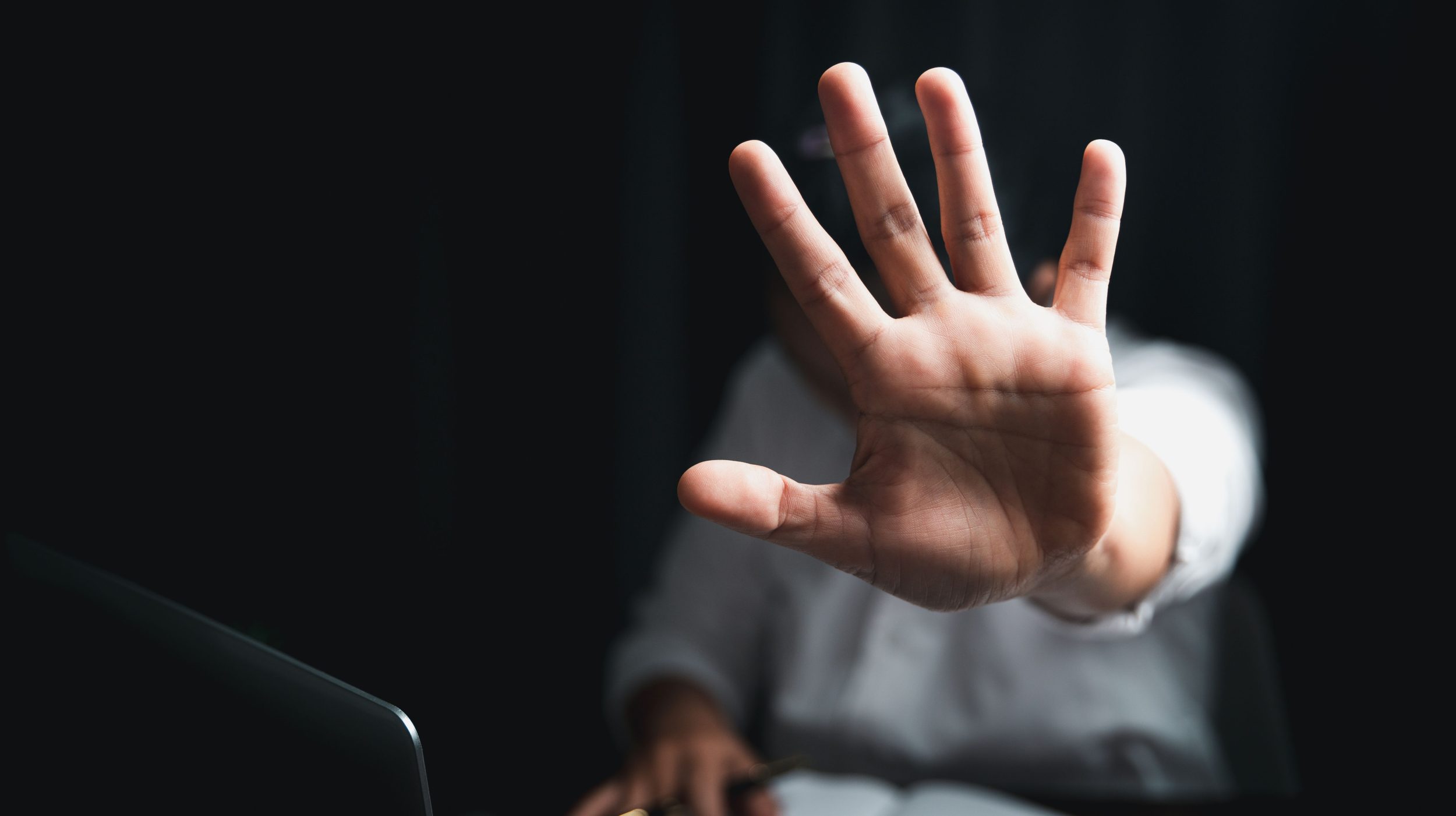 Person raising hand in a stop gesture, symbolizing barriers or resistance to reporting workplace violence concerns.