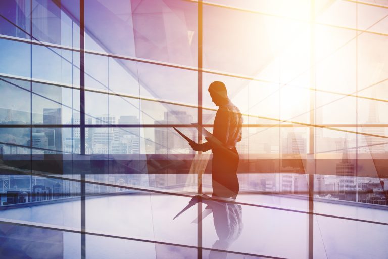 Silhouetted business professional reviewing documents in front of large windows with a city skyline